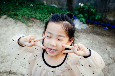 High angle view of cute girl with eyes closed showing peace sign on footpath