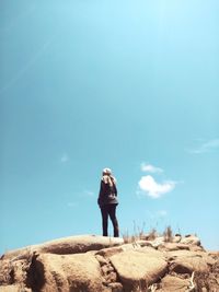 Man standing on rock against blue sky