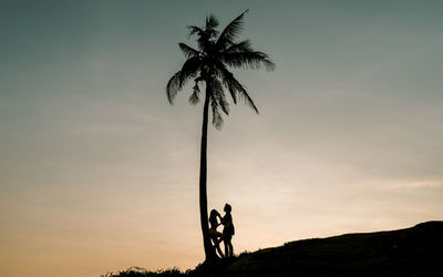 Silhouette people by palm tree against sky during sunset