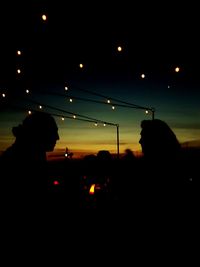 Silhouette people with illuminated lights against sky at night