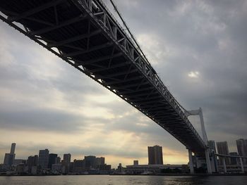 Rainbow bridge over sea by city against cloudy sky during sunset
