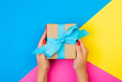 Directly above shot of cropped hands holding gift box on colored background