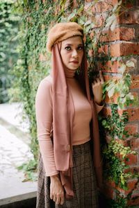 Portrait of woman standing by plants on wall