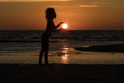 Silhouette woman standing on beach against sky during sunset