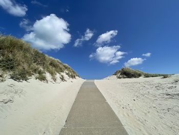 Scenic view of dunes and a pathway against blue sky