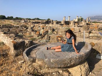 Girl eating while sitting at old ruins against blue sky