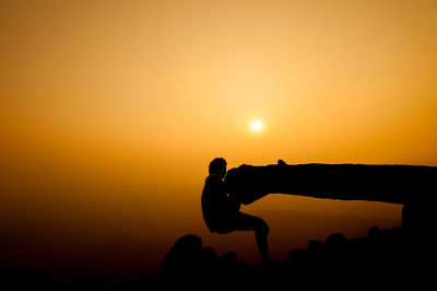 Silhouette of man rock climbing against sky during sunset