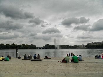 Group of people relaxing on lake against sky