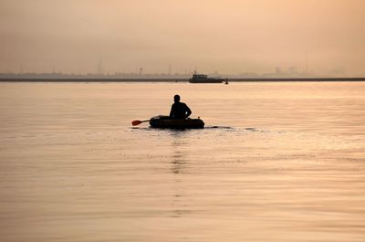 Silhouette man on boat in sea against sky during sunset