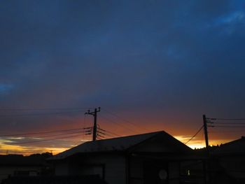 Silhouette houses and electricity pylon against romantic sky at sunset