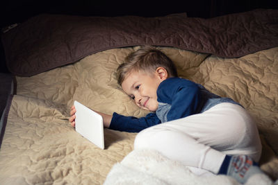 High angle view of boy using digital tablet while lying on bed at home