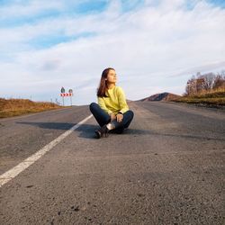 Full length of woman sitting on road against sky