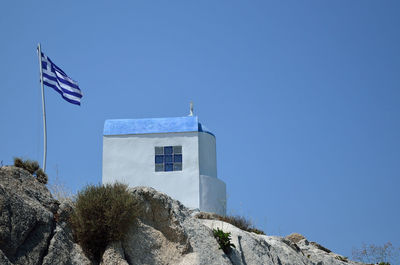 White-blue greek orthodox chapel on rock with greek flag