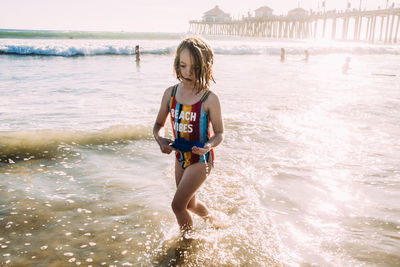 Young girl running through water at the beach with pier in background