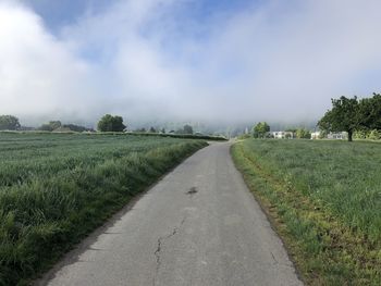 Empty road amidst field against sky