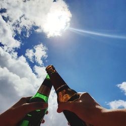 Low angle view of hand holding glass bottle against sky