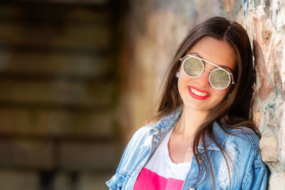 Portrait of teenage girl wearing sunglasses and denim jacket while standing by wall