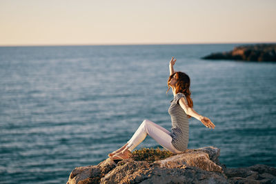 Young woman on rock by sea against sky