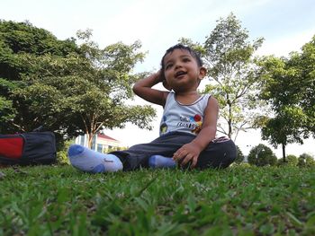 Portrait of smiling boy sitting on grass against trees