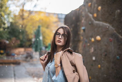 Portrait of young woman wearing jacket while standing against wall