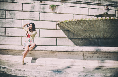 Full length of woman sitting on fountain