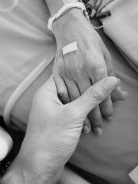 Cropped image of man holding hands with female patient on hospital bed