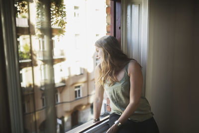 Young woman looking through window at home