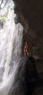 Woman standing on rock against waterfall