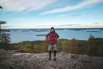 Laughing backpacker standing on rock with lake jatkonjarvi behind him in koli national park, finland