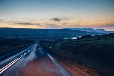 Empty country road along landscape at sunset