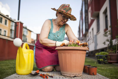 From below mature woman gardener, transfers a plant to a large flowerpot in her home garden