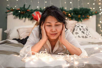 Senior asian woman relax on bed looking at xmas lights, elderly lady at christmas, atmospheric mood