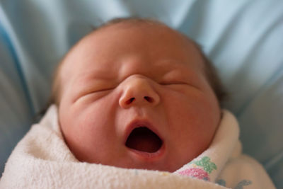 Close-up of baby boy yawning while sleeping on bed