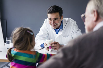 Doctor and happy girl with grandfather at desk in medical practice