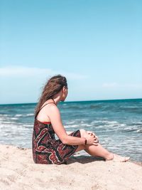 Young woman sitting on beach against clear sky