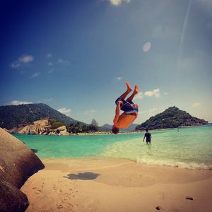 Shirtless man backflipping at beach on sunny day