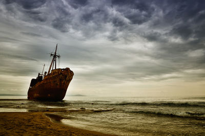 Abandoned sailboat on sea shore against sky
