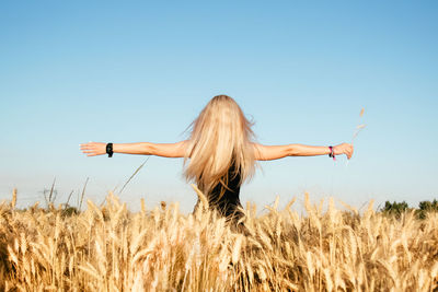 Rear view of woman standing on field against clear blue sky