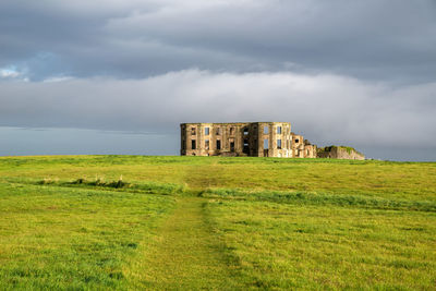 Old ruin building in field against cloudy sky