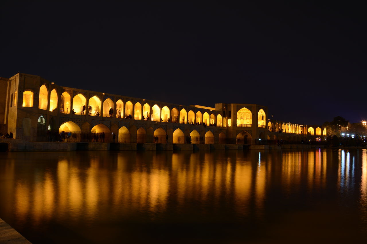 REFLECTION OF ILLUMINATED BRIDGE OVER RIVER AT NIGHT