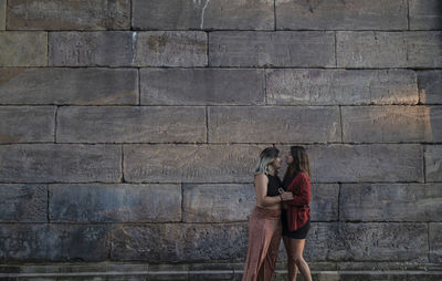 Portrait of two girls standing against stone wall