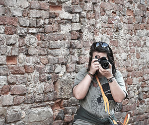 Woman photographing while standing against brick wall