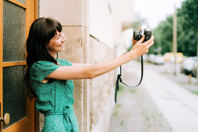 Side view of woman photographing while standing outdoors