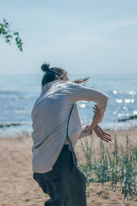 Rear view of woman standing at beach against sky