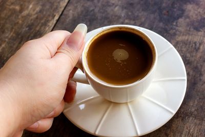 Close-up of hand holding coffee cup on table