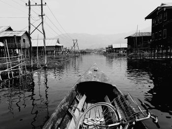 Bicycle in boat amidst stilt houses against sky