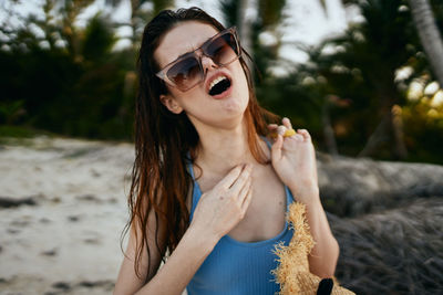 Portrait of smiling young woman wearing sunglasses while standing at beach