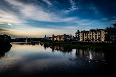 Buildings by river against sky in city at dusk