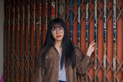 Portrait of young woman standing by metallic gate