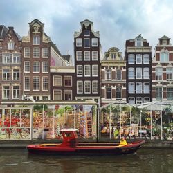 Boat passing by amsterdam flower market in canal against buildings in city